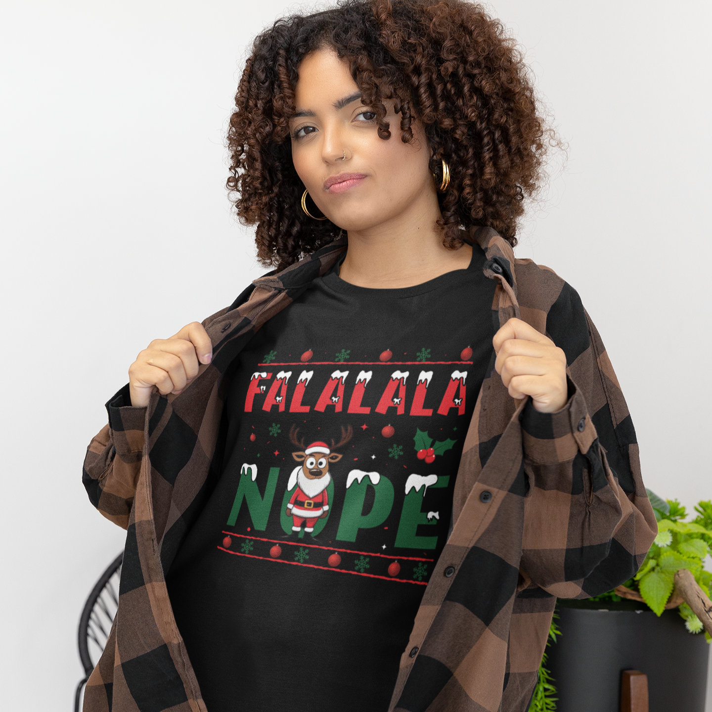 Person wearing a black t-shirt with 'FALALALA NOPE' text, holding a plaid jacket indoors.