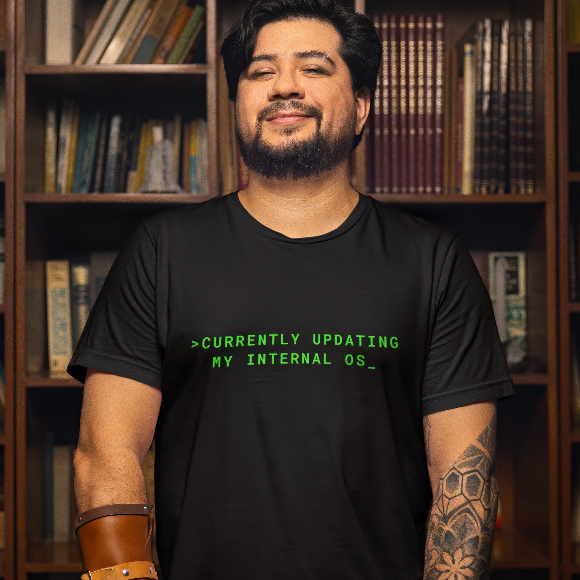 Man wearing a black t-shirt with green text in front of a bookshelf