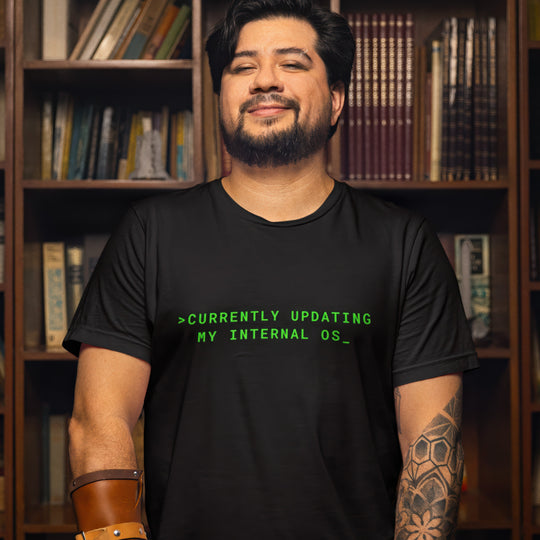 Man wearing a black t-shirt with green text in front of a bookshelf