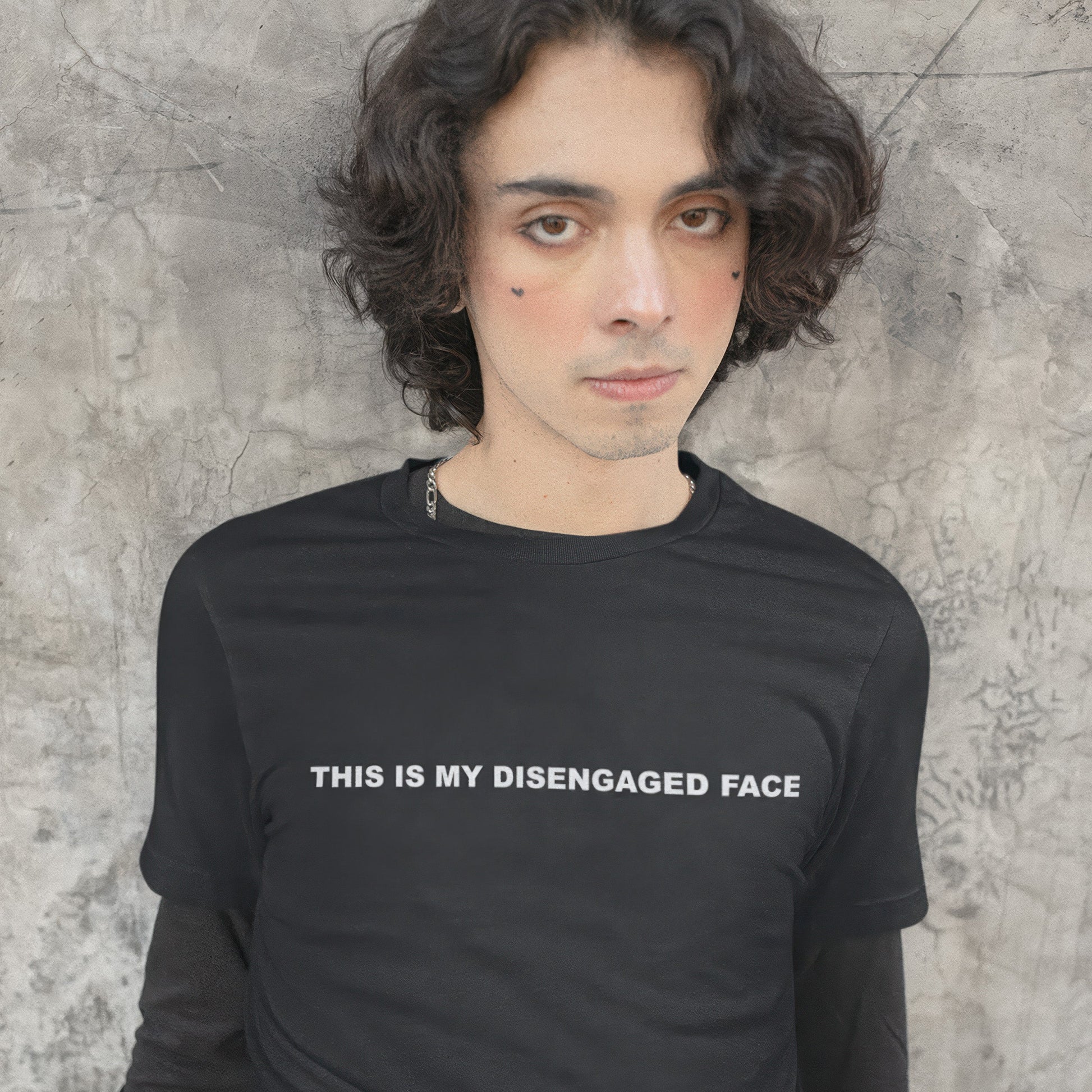 Person wearing a black t-shirt with text 'THIS IS MY DISENGAGED FACE' against a textured wall.