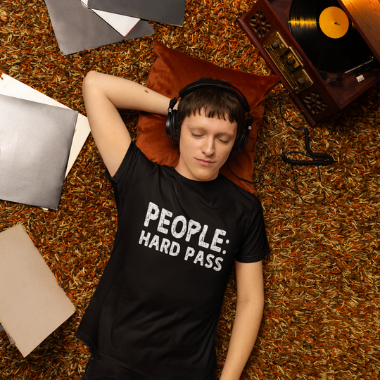 Person wearing headphones and a black t-shirt with text, lying on a carpeted floor next to a record player.