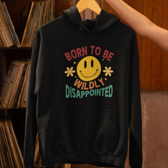 Black hoodie with colorful text and smiley face graphic on a hanger against a bookshelf background