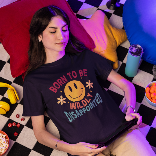 Person wearing a t-shirt with a colorful graphic and text, lying on a checkered floor with snacks and drinks.