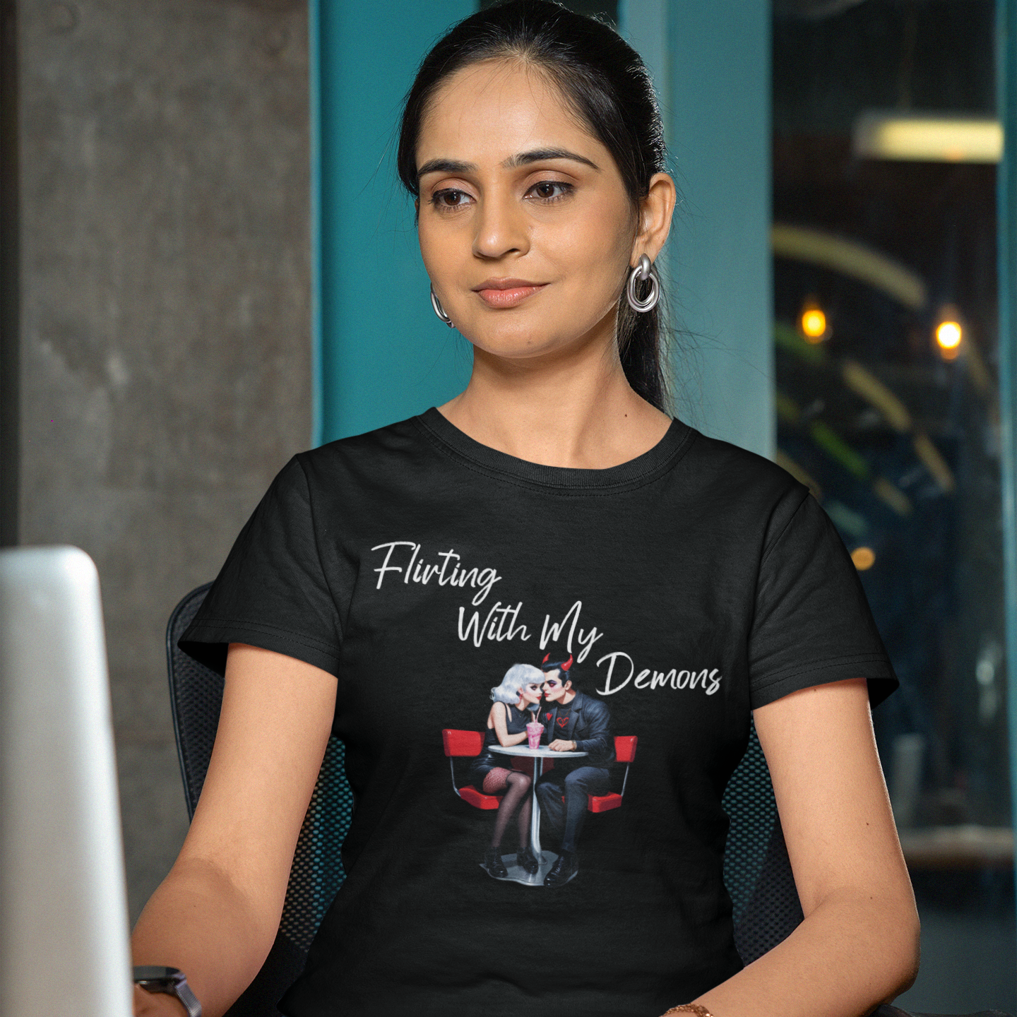 Woman wearing a black t-shirt with text and graphic, sitting at a desk with a laptop.