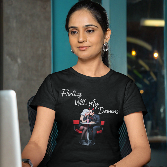 Woman wearing a black t-shirt with text and graphic, sitting at a desk with a laptop.