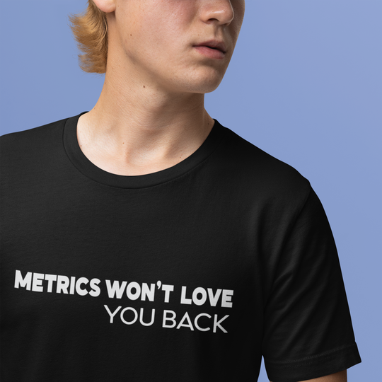 Person wearing a black t-shirt with 'METRICS WON'T LOVE YOU BACK' text against a blue background